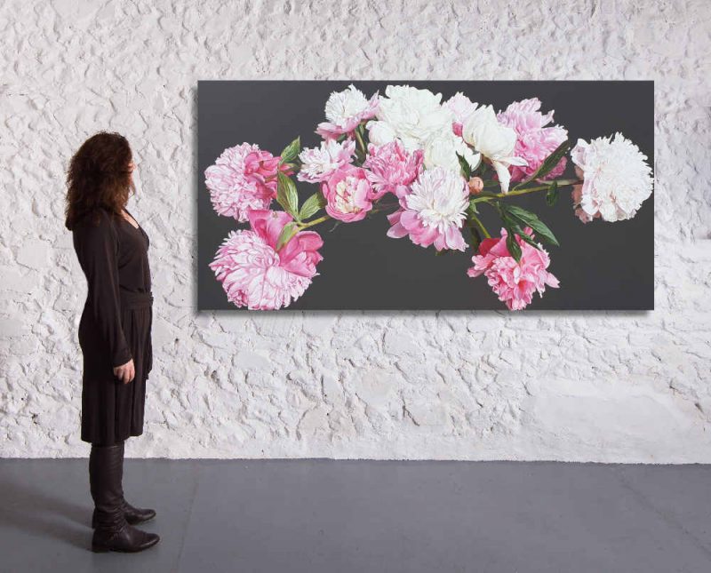 Original acrylic painting on brown background by Sarah Caswell of pink peonies in bright sunshine. Shown in a gallery setting.