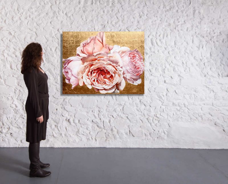 Original acrylic painting by Sarah Caswell of Coral pink David Austin ‘Jubilee Celebration’ roses in bright sunshine on red gold. Shown in a gallery setting.